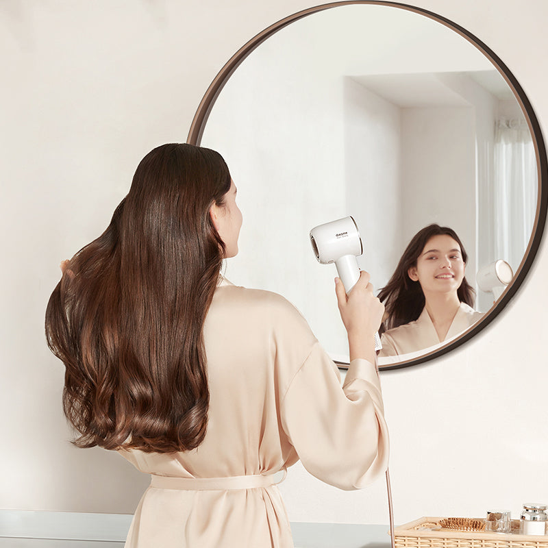 Woman using Dreame Hair Glory high-speed hair dryer in front of a round mirror.