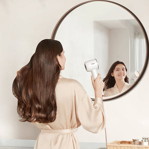 Woman using Dreame Hair Glory high-speed hair dryer in front of a round mirror.